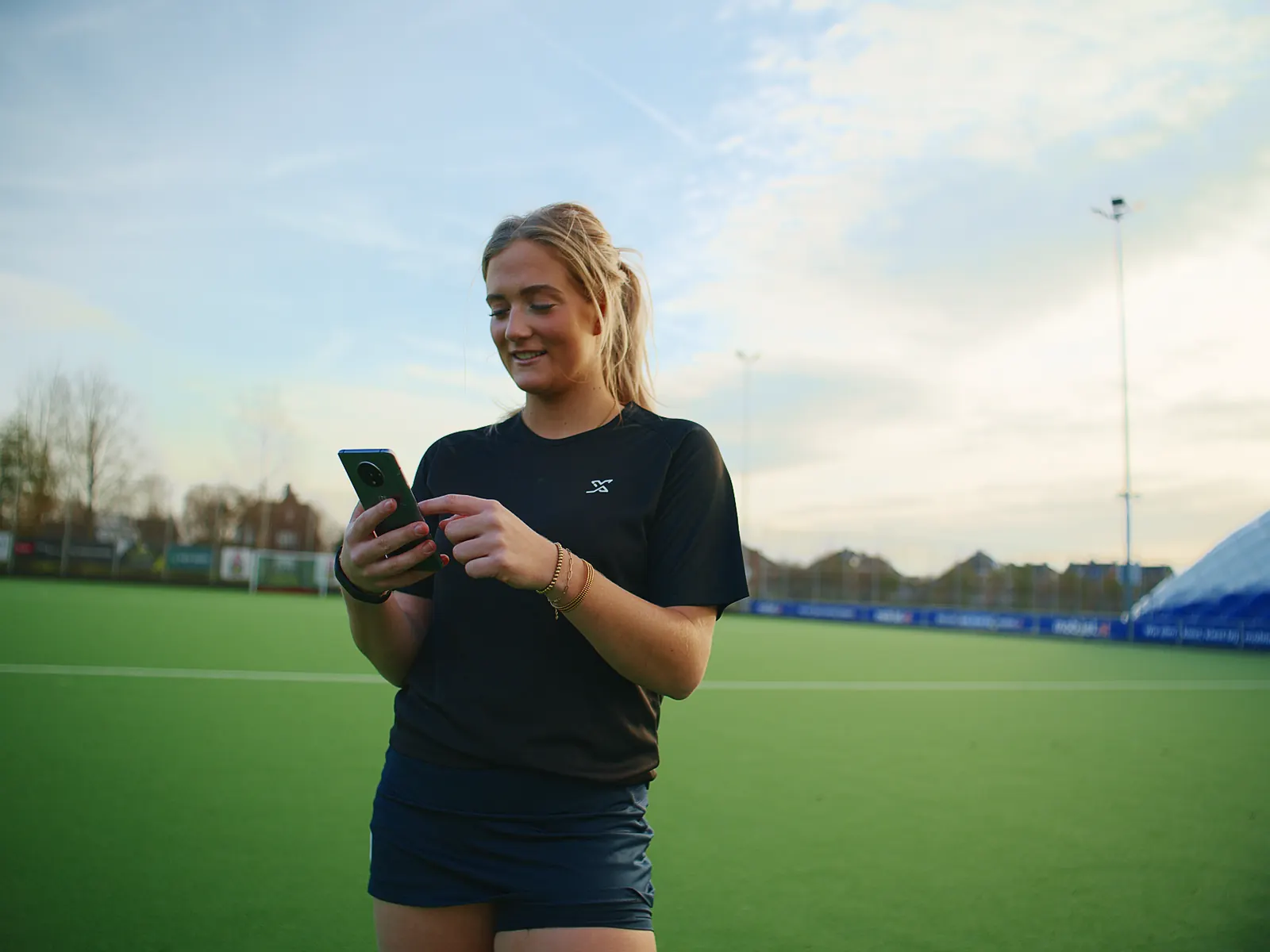 Hockey player checking her score in the app beside the pitch